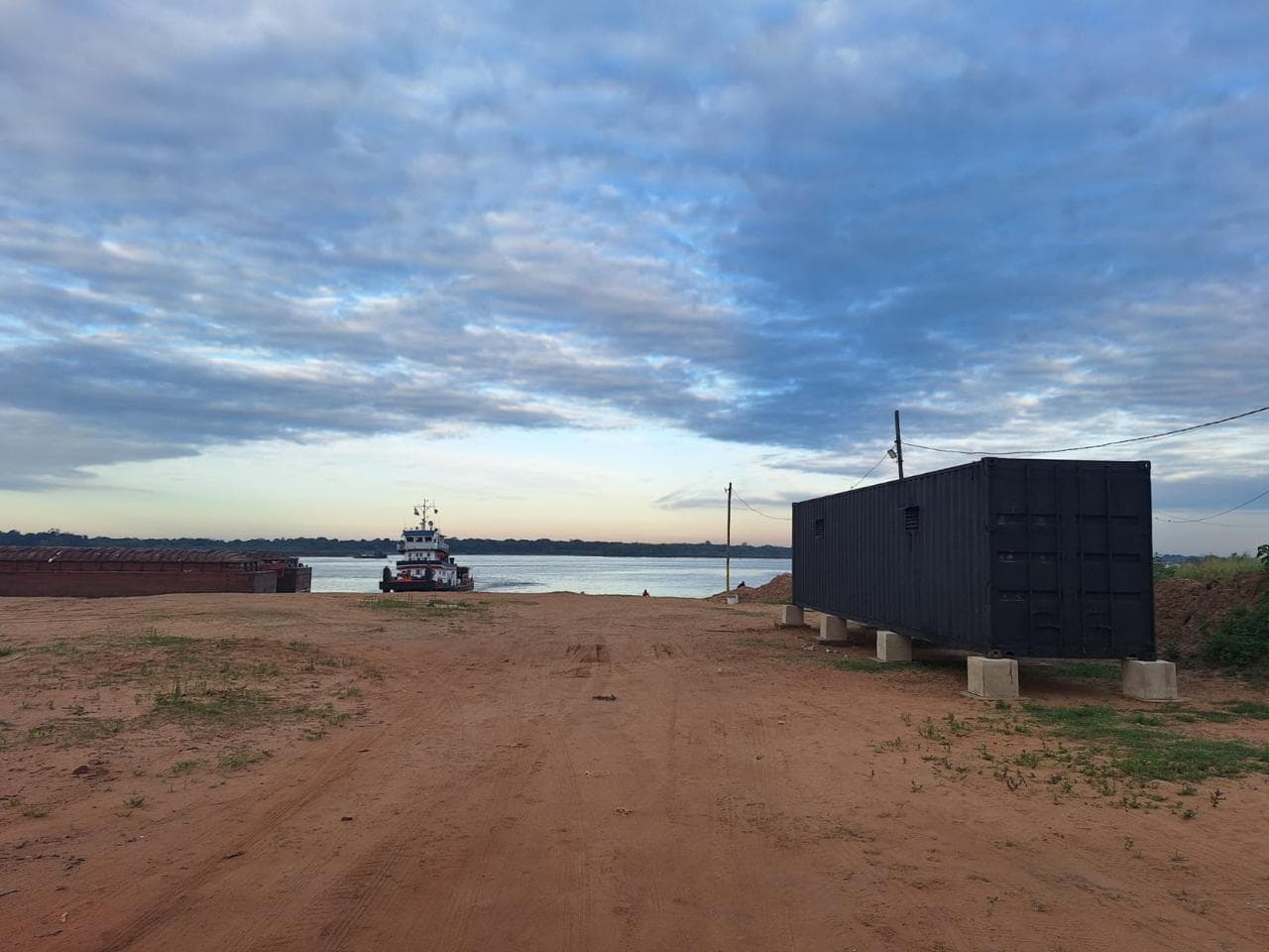 Explanada de acceso al puerto al atardecer con un remolcador y barcazas sobre el río